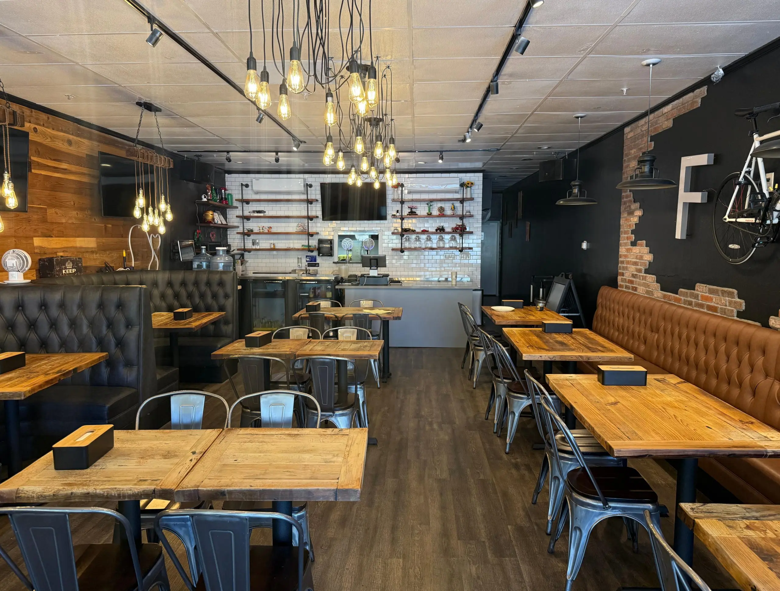 Modern industrial-style restaurant interior with wooden tables, leather booths, and exposed light bulbs.